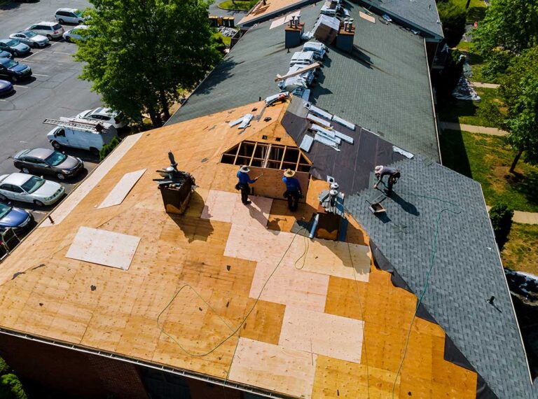 Attic inspection showing stained roof decking, insulation, rafters, and a flashlight in a homeowner’s hand.