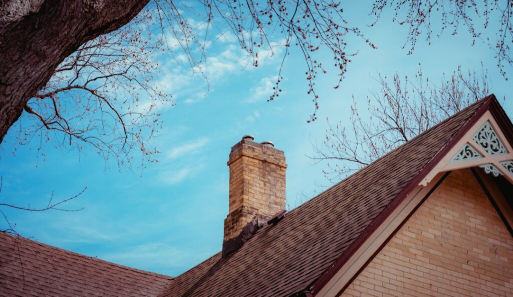Roof inspector examining damaged shingles and flashing beside a ceiling water stain inside a home.